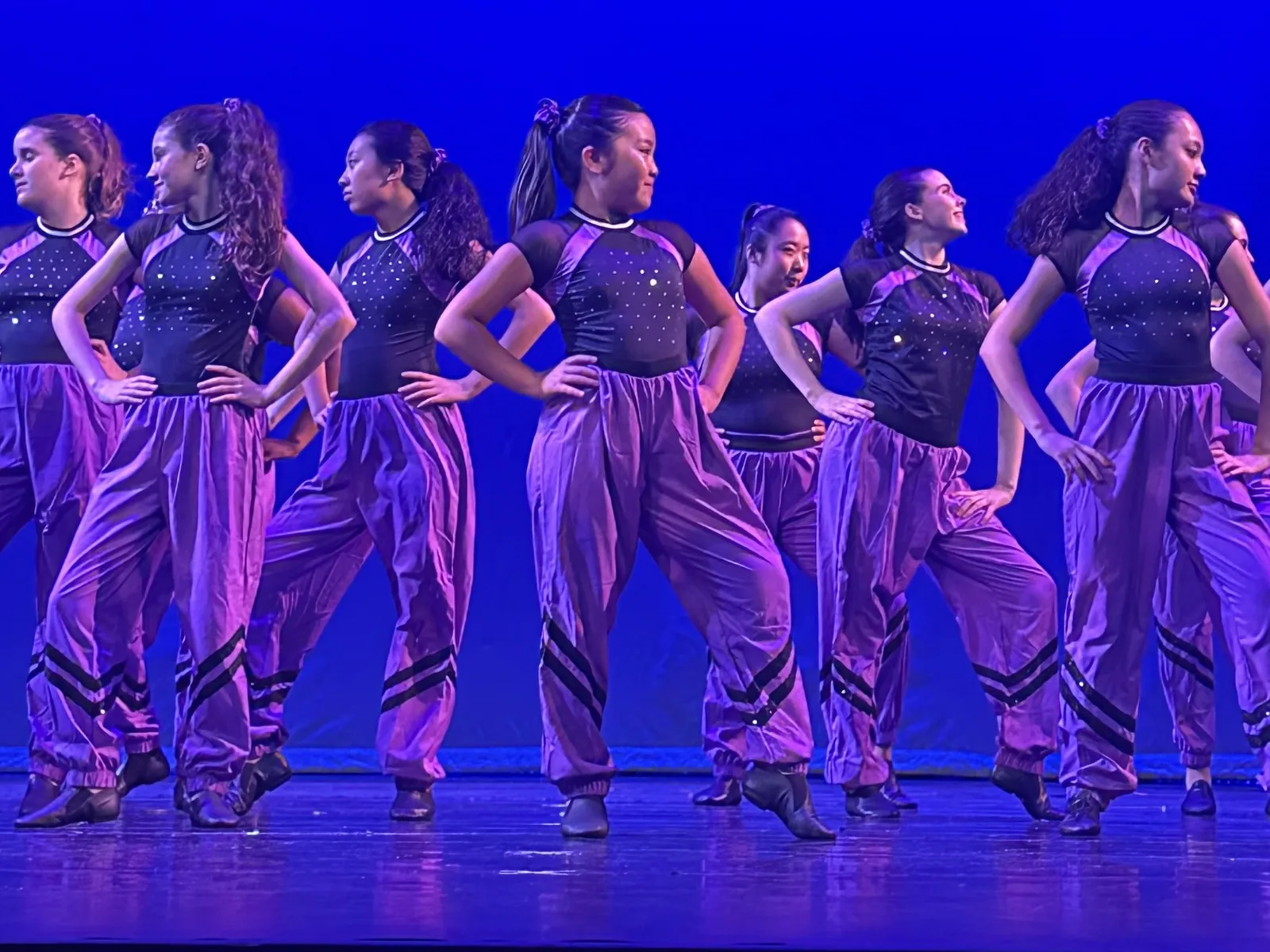 jazzl dance crew in purple pants and sparkle tops posing on stage