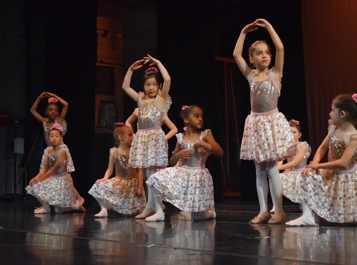 Young ballet dancers in sequin tutus perform on stage in fifth position