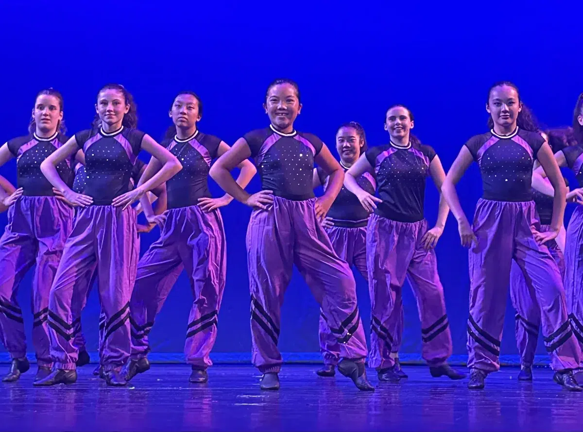 Commercial Dance students in purple costumes pose together on stage