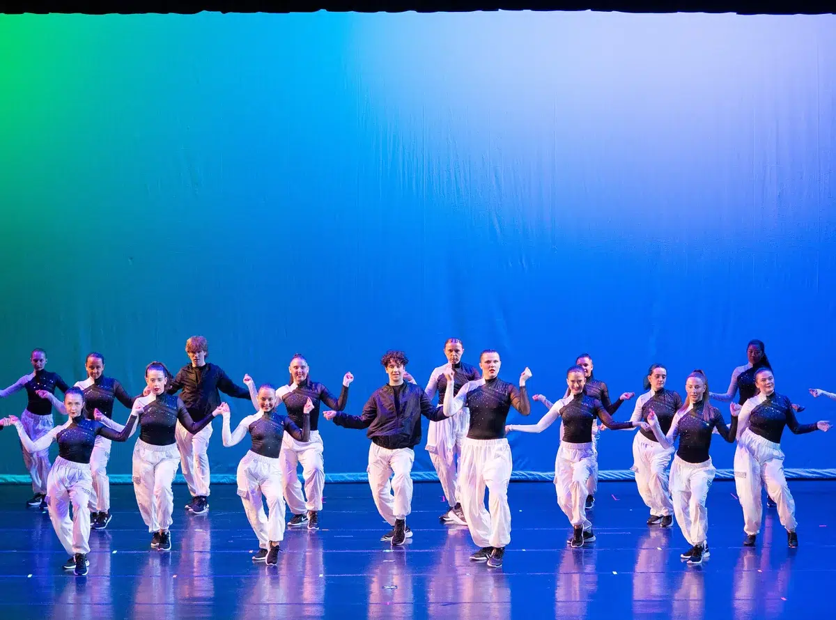 Commercial Dance students in black tops and white pants perform on stage