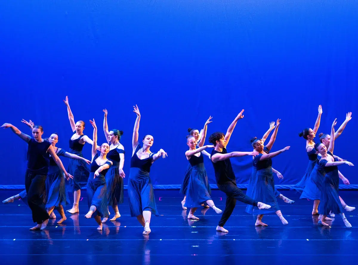 Contemporary dancers in flowing skirts perform barefoot on a blue-lit stage