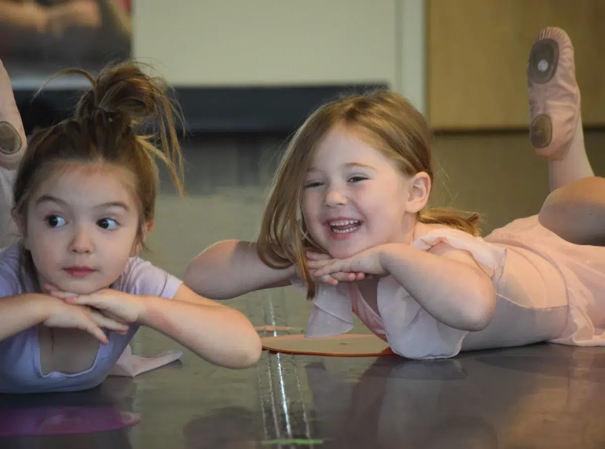 Two young dancers lie on the studio floor laughing together during class