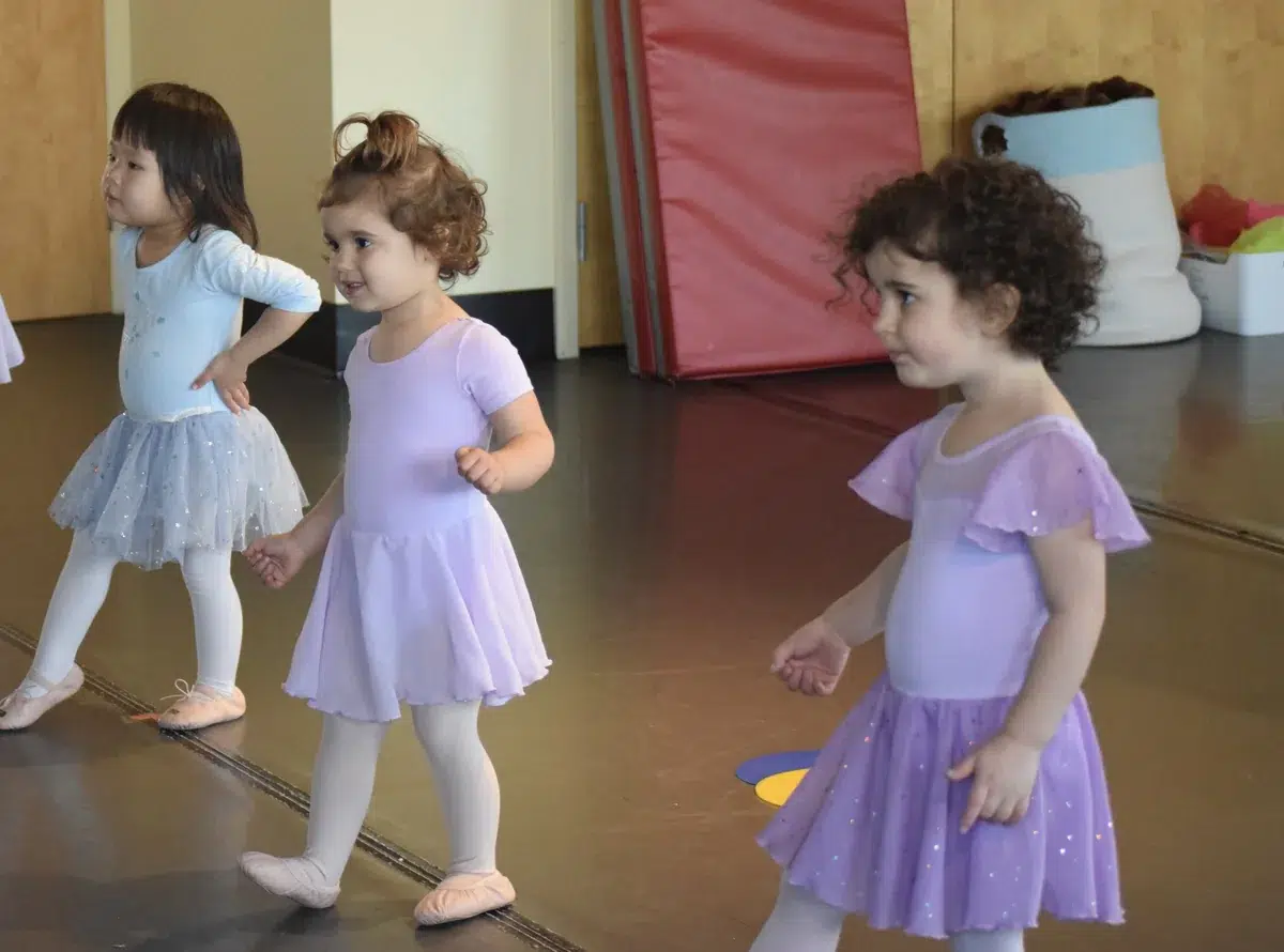 Toddlers in leotards march across the studio during an early childhood ballet class