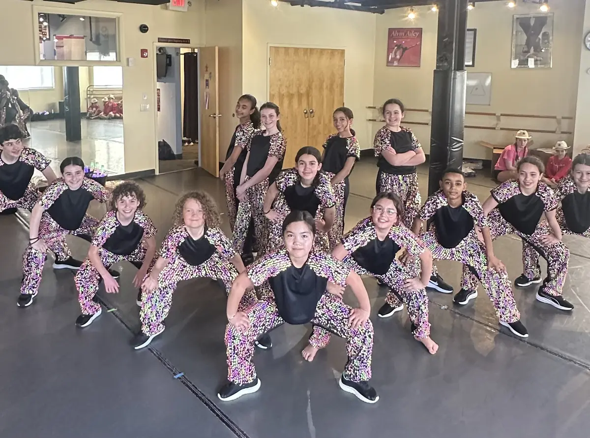 Hip Hop dancers in sequined costumes hold a wide stance pose in the studio