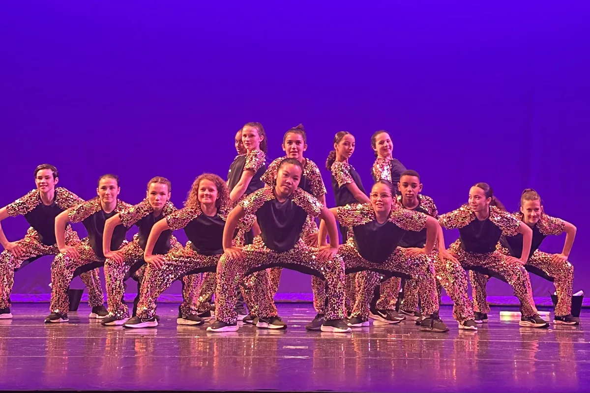 Hip hop dancers in gold sequin costumes posed on a purple-lit stage