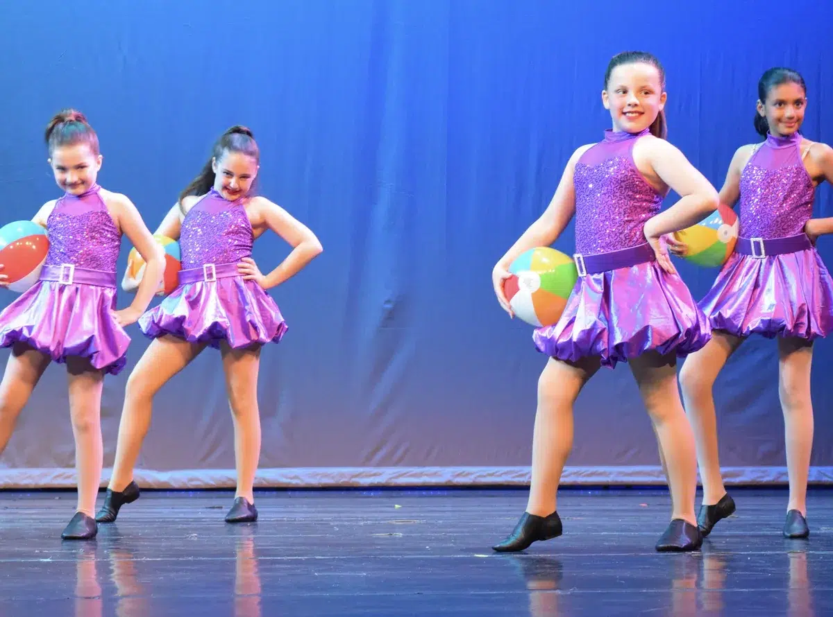 Young jazz dancers in purple costumes perform on stage with beach balls