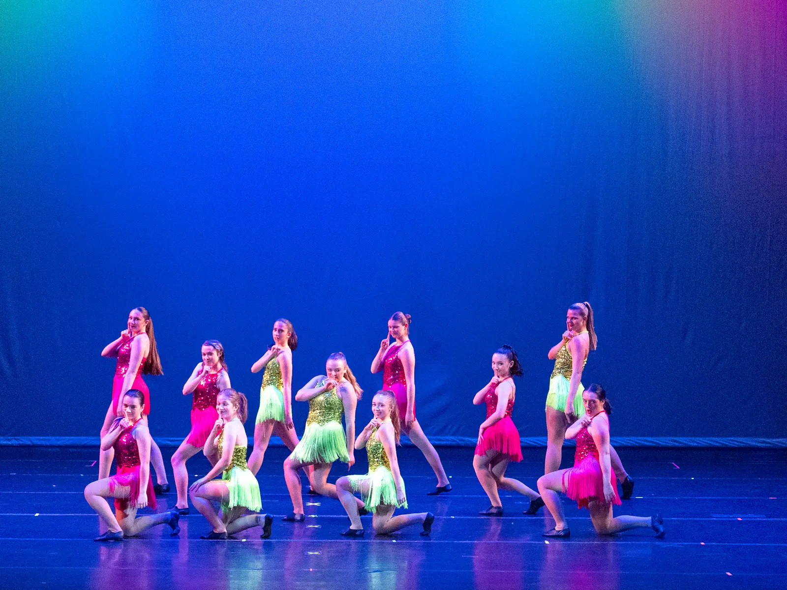 Jazz Fusion dancers in pink and green fringe costumes perform on stage