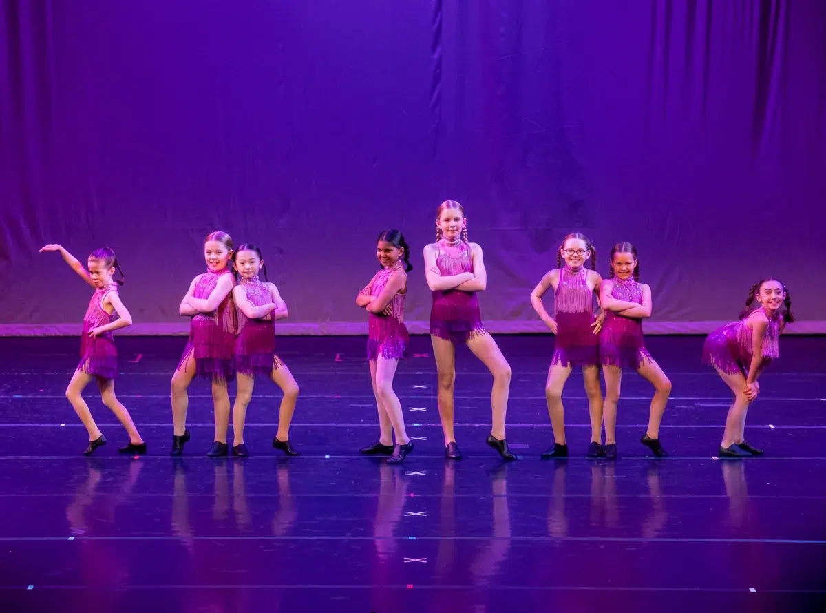 Young dancers in magenta fringe costumes perform on stage in tap shoes