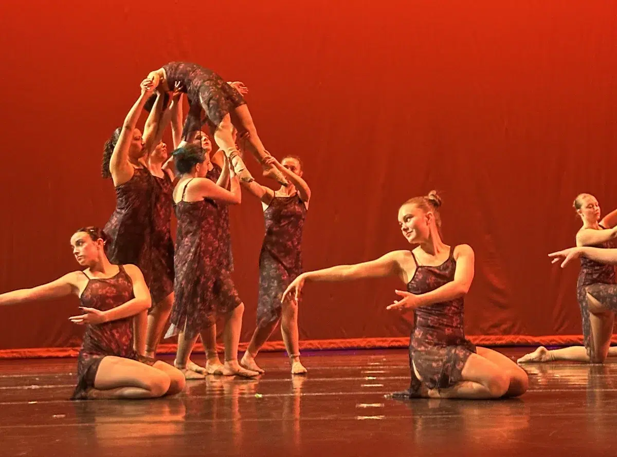 Teen lyrical dancers perform on stage in floral costumes with an overhead lift behind them
