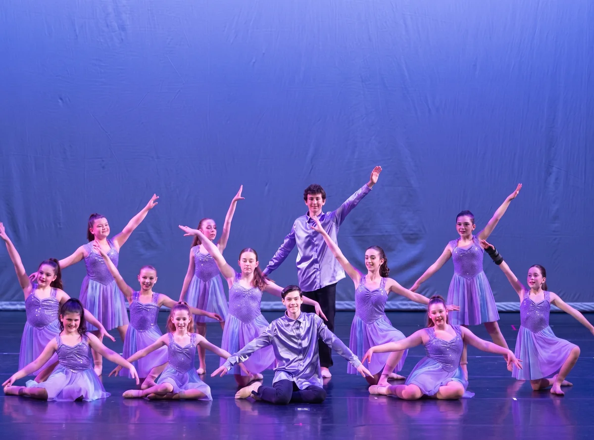 Lyrical dancers in lavender dresses hold a group pose on stage