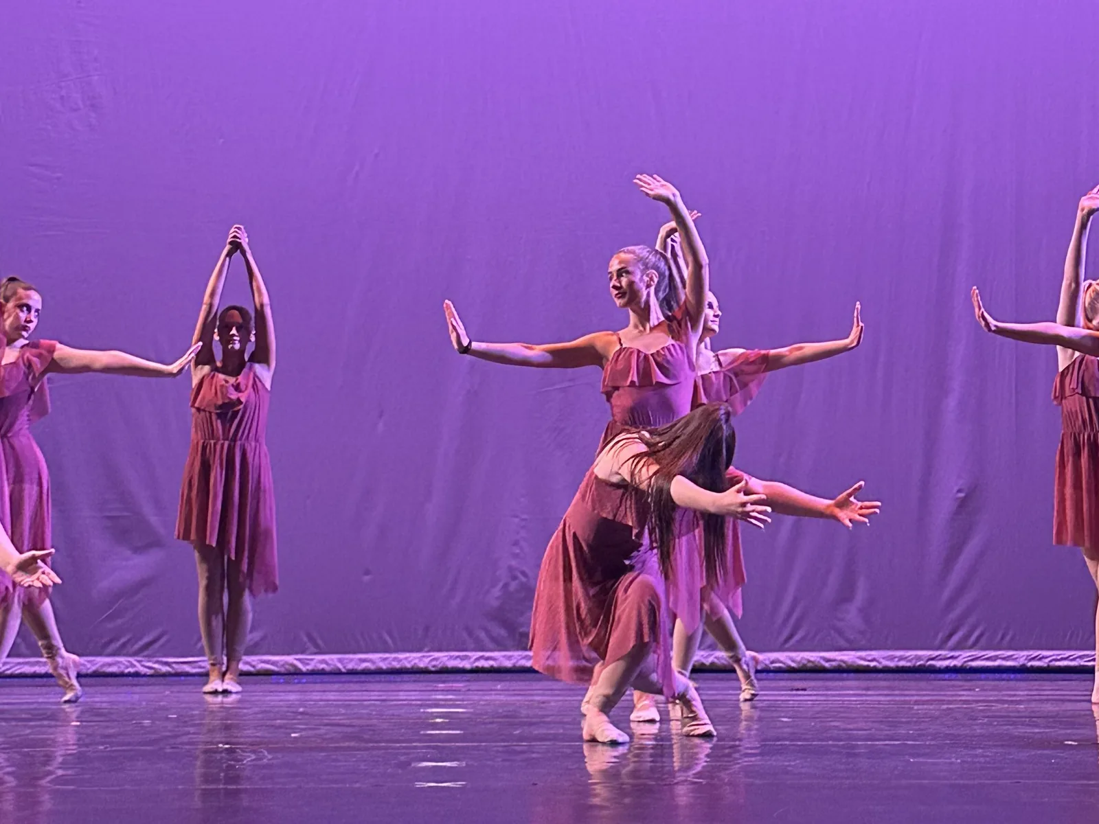 Lyrical dancers in rose costumes perform an expressive group number on stage