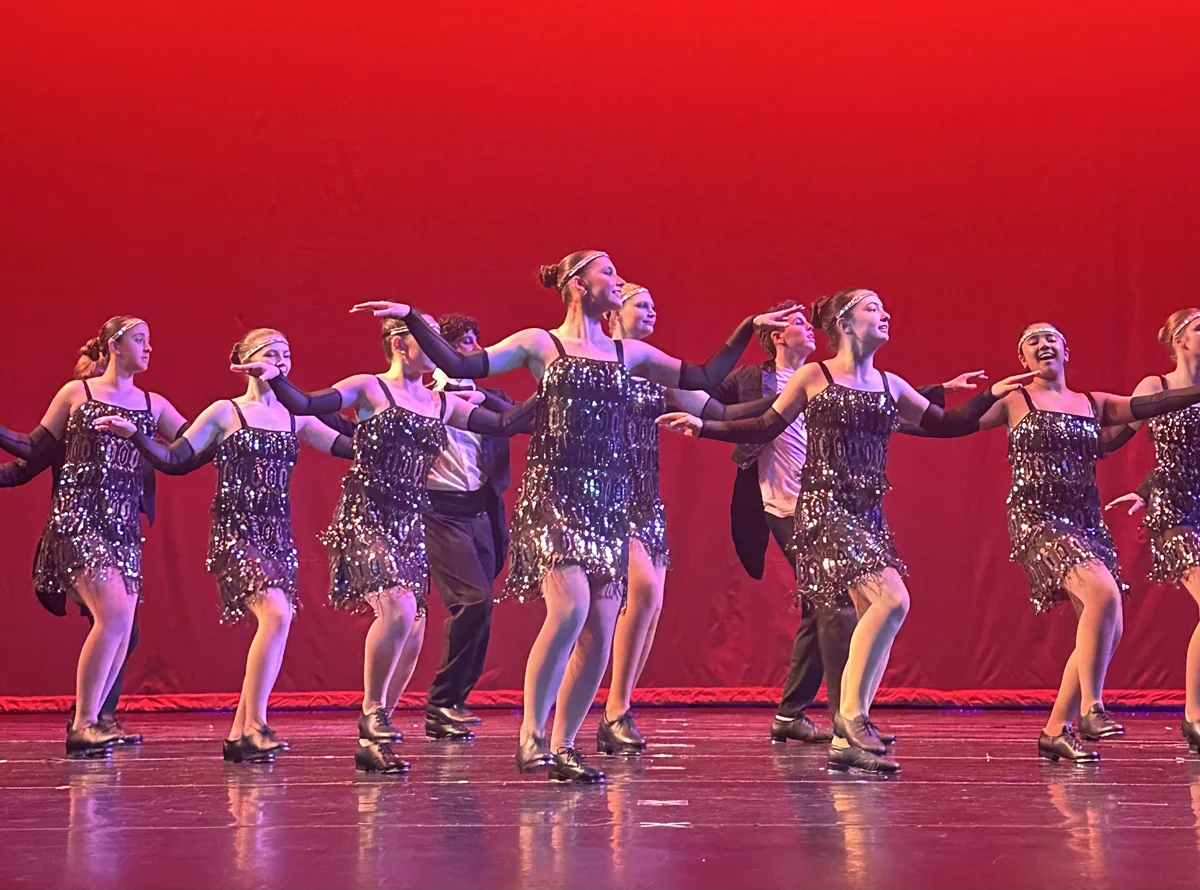 Teen tap dancers in silver fringe costumes perform on stage in tap shoes