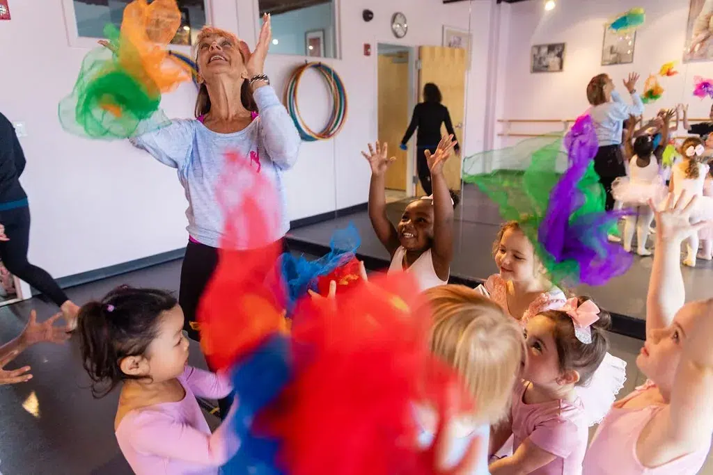 Young dancers reach up to catch brightly coloured scarves during a creative movement class