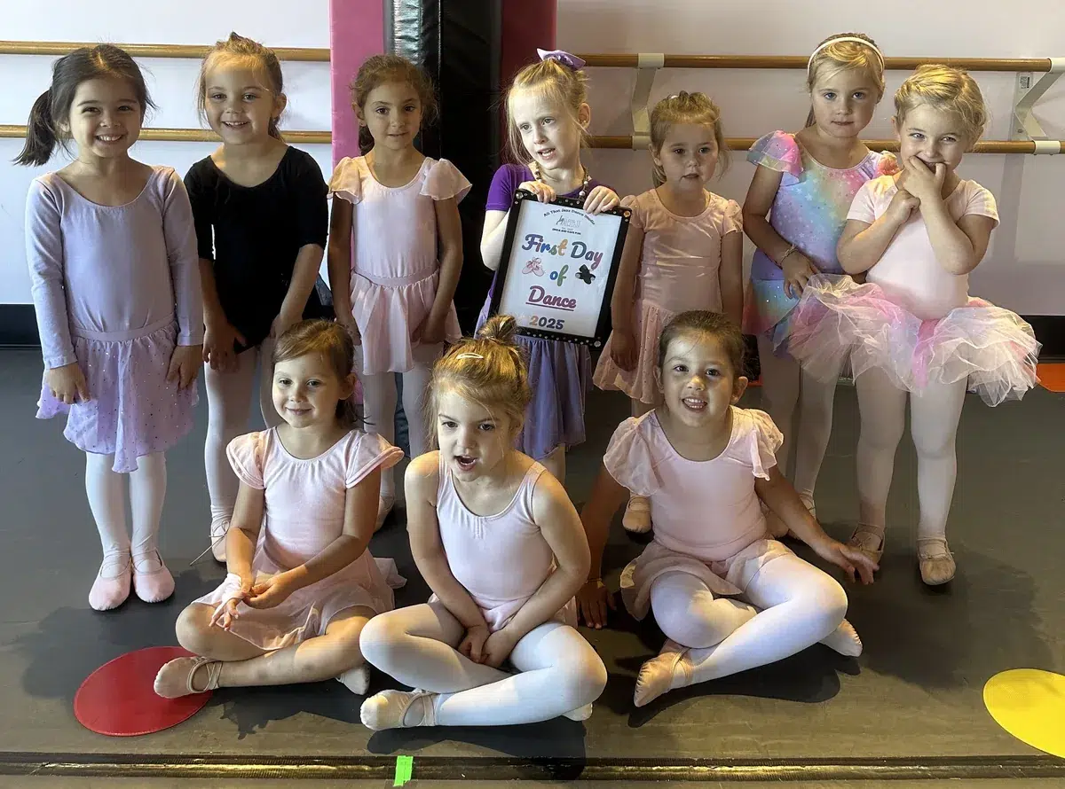 Young dancers gathered around a First Day of Dance sign in a Mini Movers class at All That Jazz Dance Studio